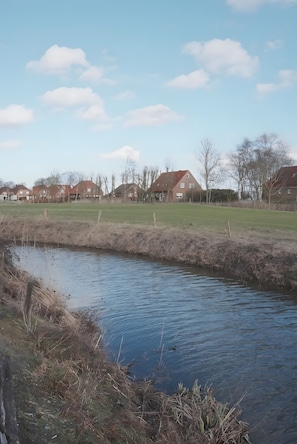 Ein ruhiges Gewässer mit Uferwiese, umgeben von Häusern mit roten Dächern.