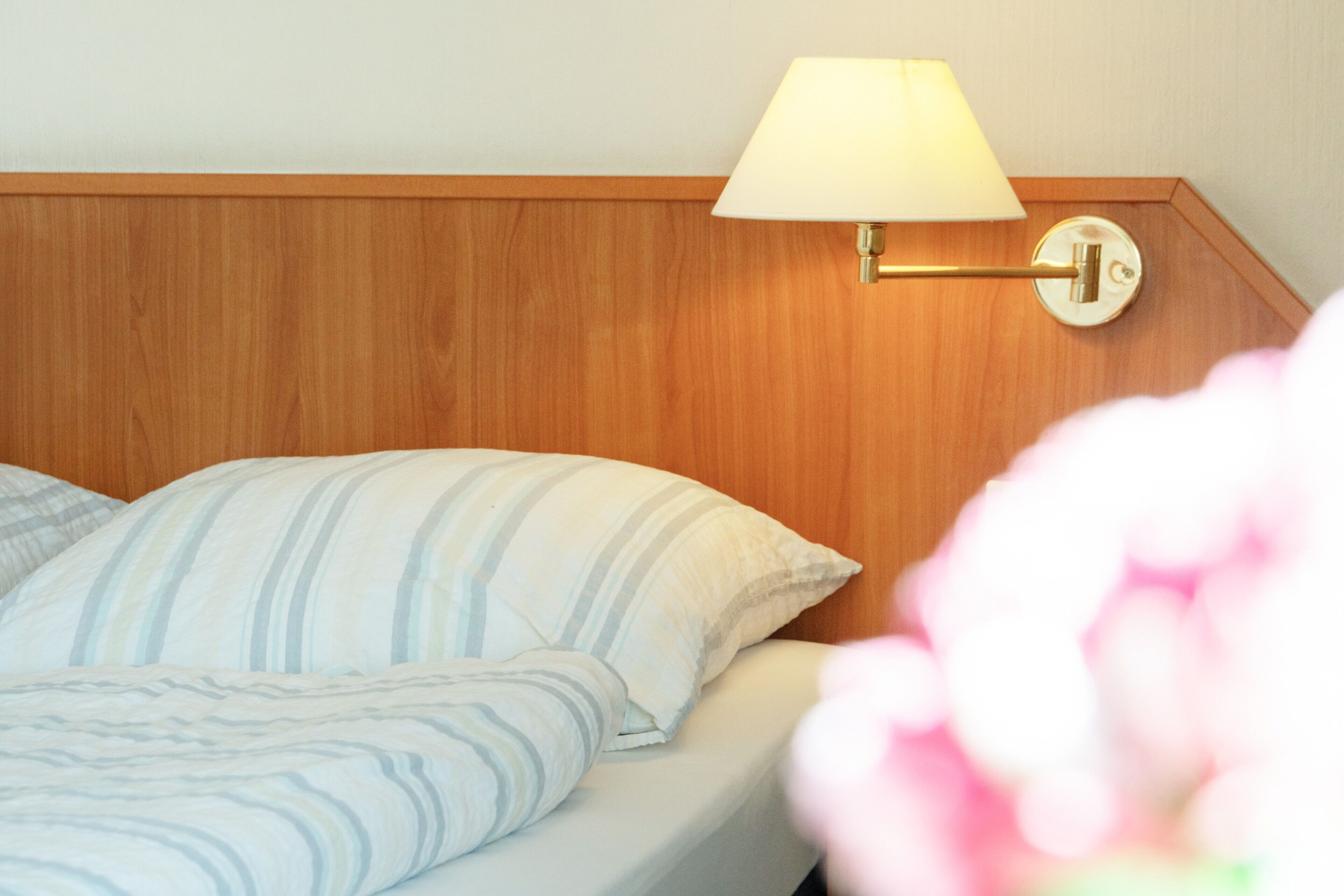 Une chambre d’hôtel avec une tête de lit en bois, un lit avec une literie à rayures et une lampe fixée au mur.