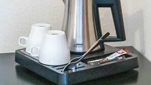 A coffee maker with two white cups on a tray.