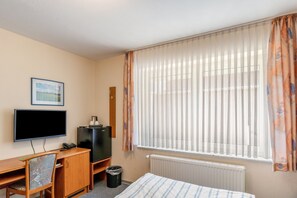 Habitació d'hotel amb llit, escriptori, ordinador, cadira, televisió i finestra amb cortines.
