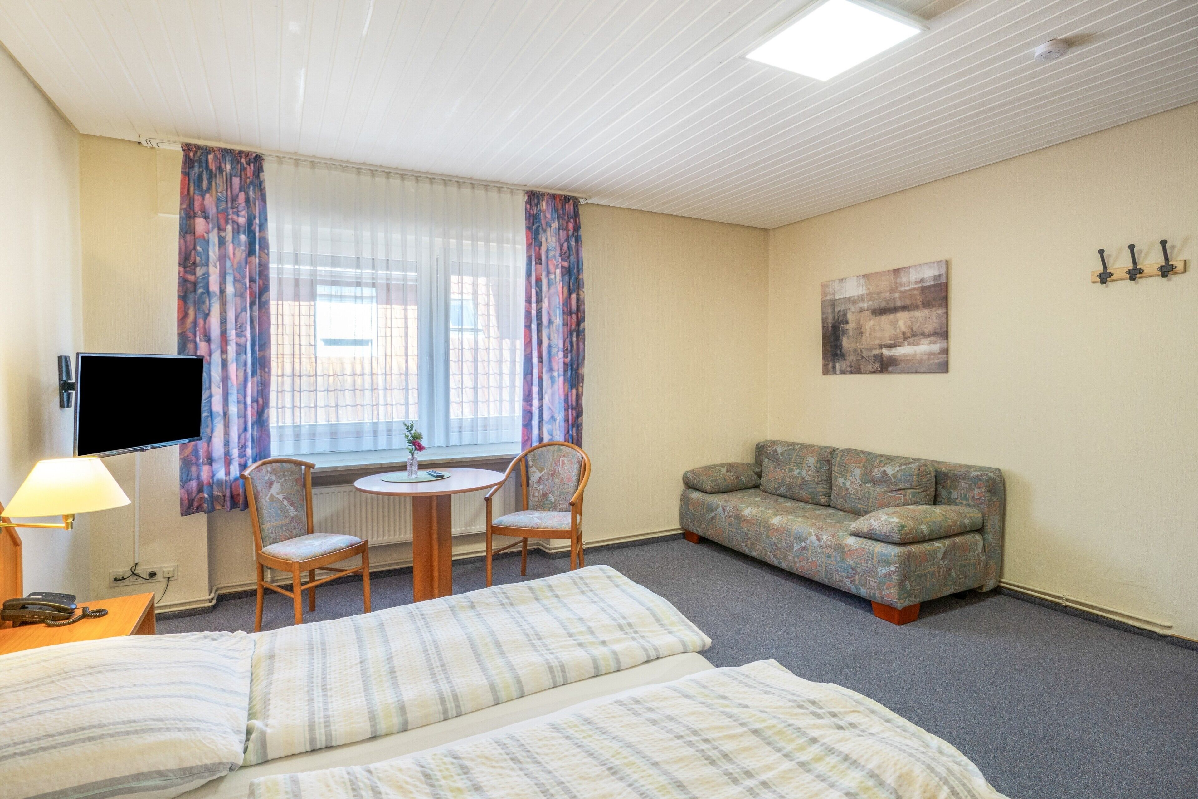 Ein Hotelzimmer mit Bett, einer Couch, einem Tisch mit Stühlen, einem Fernseher und einem Fenster mit Vorhängen.