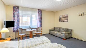 Ein Hotelzimmer mit Bett, einer Couch, einem Tisch mit Stühlen, einem Fernseher und einem Fenster mit Vorhängen.