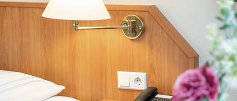 A hotel room with a wooden headboard, a bedside lamp, a telephone, and a power outlet.