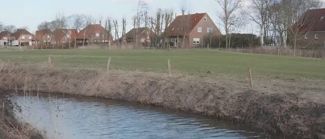 A calm water body with a grassy bank, surrounded by houses with red roofs.
