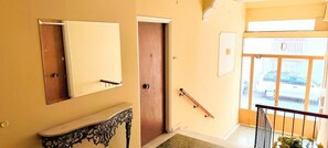 A hallway with a mirror, a door, a coat rack, and a view of parked cars through a window. - Cozy apartment in Acropolis (Athens)