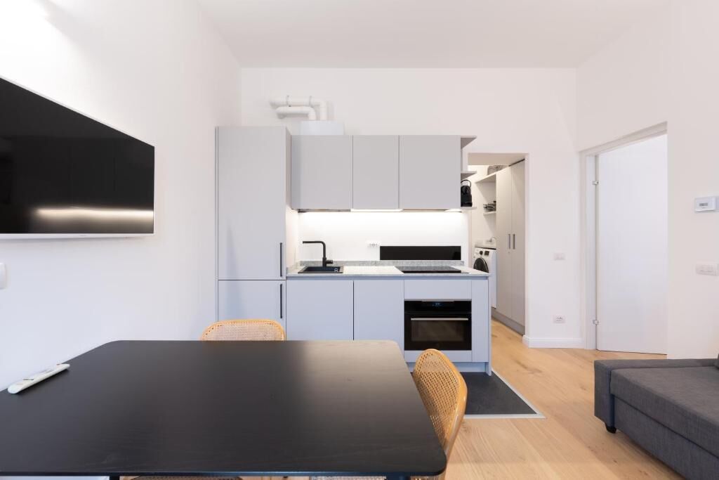 Eine moderne Küche mit grauen Schränken, einer schwarzen Arbeitsplatte und einem Essbereich mit einem schwarzen Tisch und Korbstühlen.