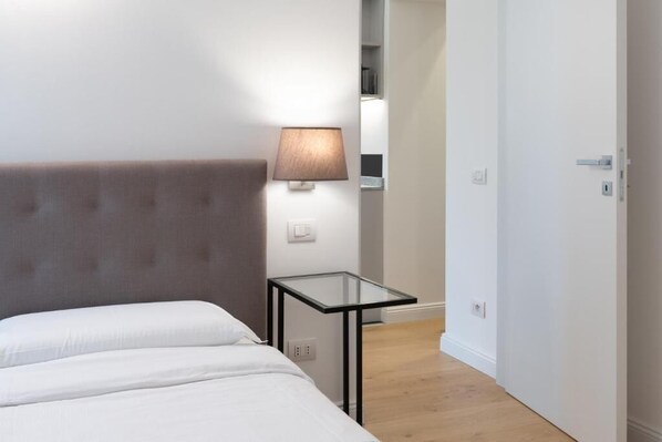 Una habitación de hotel con una cama, una mesita de noche, una lámpara y una puerta.