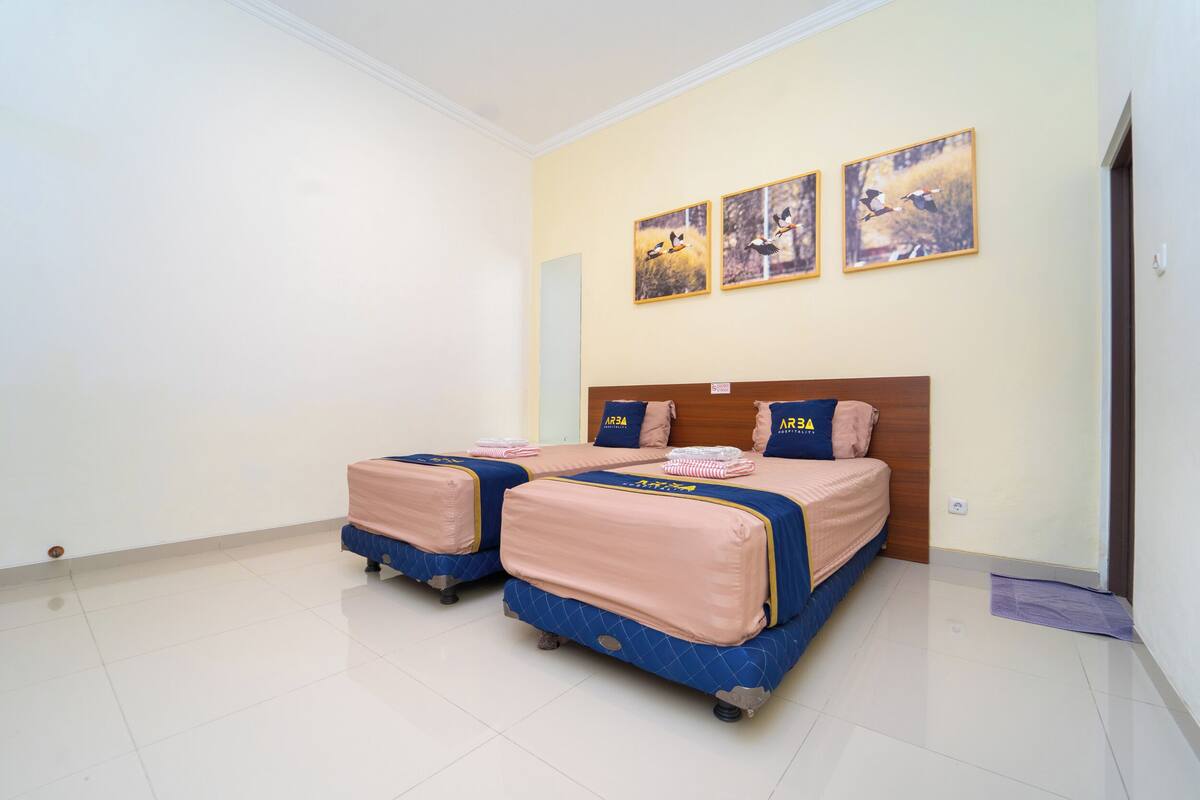 A hotel room with two beds, a wooden headboard, and three wall-mounted pictures.