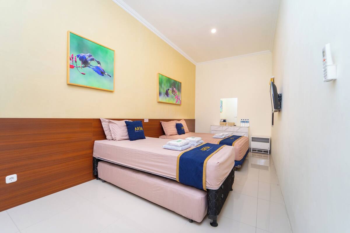 A hotel room with two beds, a wooden headboard, a white wall, and two paintings.