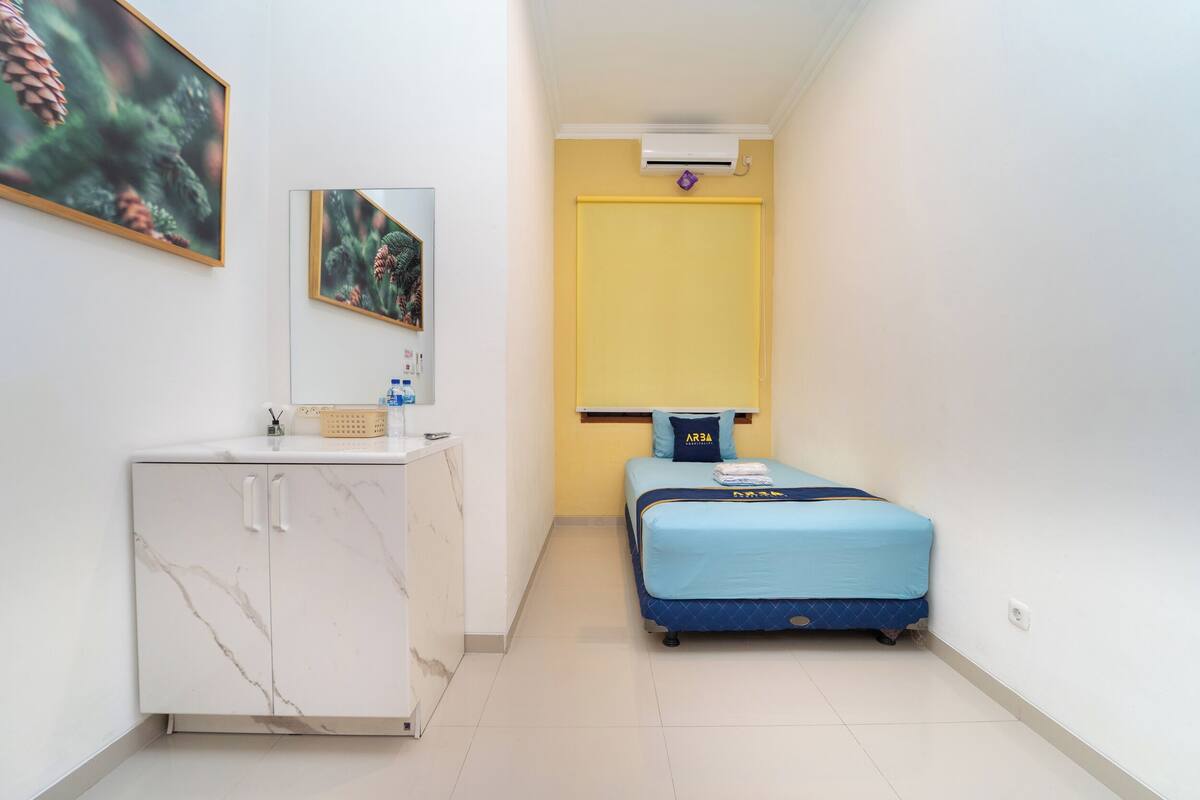 A small, compact room with a bed, a white marble cabinet, a mirror, and a yellow door.