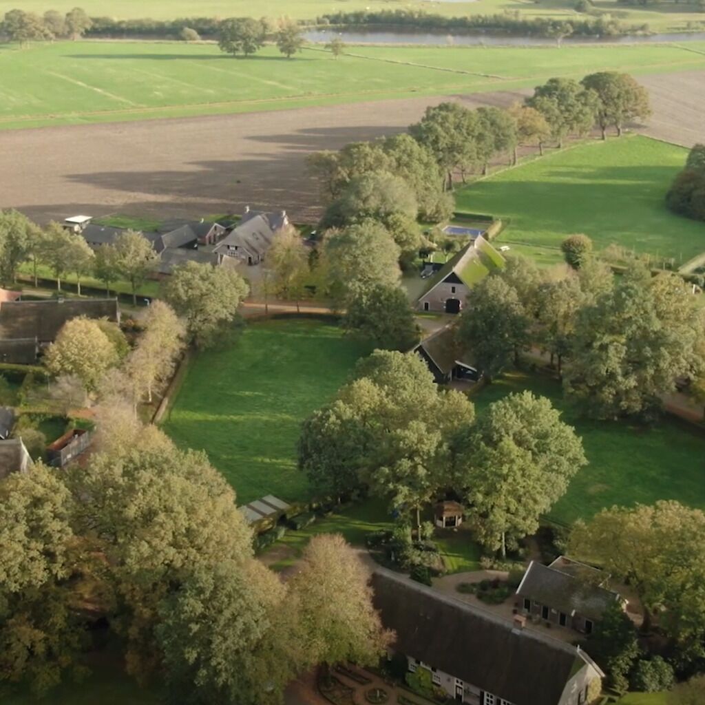 An aerial view of a rural property with multiple buildings, green fields, and trees.