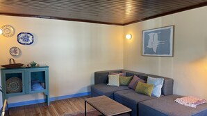 A cozy living room with a wooden ceiling, a blue sofa with cushions, a small table, and decorative plates on the wall. - 2 bedroom house in the heart of the Serra d'Aire e Candeeiros natural park (Rio Maior)