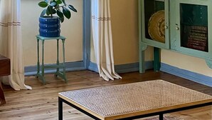 A room with a window, a potted plant, a table, and a cabinet with decorative plates. - 2 bedroom house in the heart of the Serra d'Aire e Candeeiros natural park (Rio Maior)
