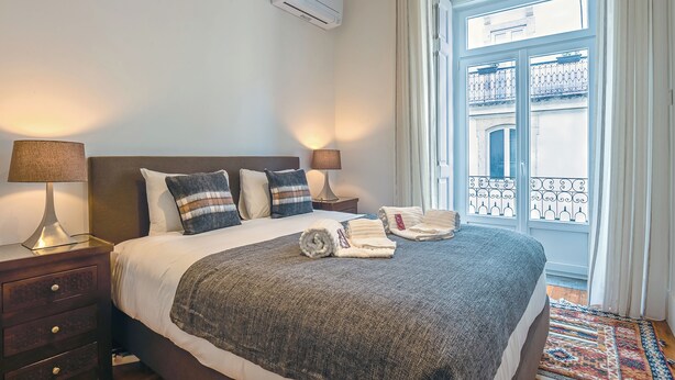 A hotel room with a bed, nightstands, a window with a view, and an air conditioning unit. - MyPlaceLisbon - Luxury Trindade II (Lisboa)