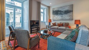 A living room with a sofa, armchairs, a coffee table, a TV, and a large abstract painting on the wall. - MyPlaceLisbon - Luxury Trindade II (Lisboa)