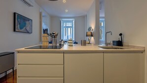 A modern kitchen with a large island, a built-in oven, and a window providing natural light. - MyPlaceLisbon - Luxury Trindade II (Lisboa)