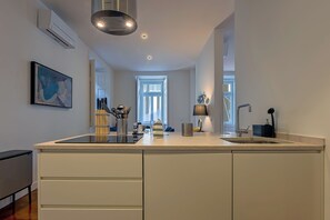 A modern kitchen with a large island, a built-in oven, and a window providing natural light. - MyPlaceLisbon - Luxury Trindade II (Lisboa)
