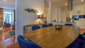 A modern dining area with a wooden table, blue chairs, and a kitchen in the background. - MyPlaceLisbon - Luxury Trindade II (Lisboa)