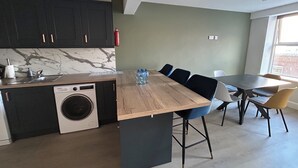 Een moderne keuken met een ingebouwde wasmachine, een eethoek met stoelen en een groot raam.