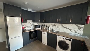 Een moderne keuken met donkere kastjes, een roestvrijstalen koelkast, een magnetron, een oven, een vaatwasser en een wasmachine.
