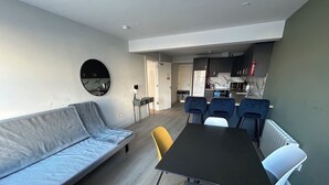 Een moderne woonkamer met een bank, een eettafel met stoelen, een keuken op de achtergrond en een grote spiegel aan de muur.
