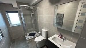 Een moderne badkamer met een glazen douchecabine, toilet, wastafel en spiegel.