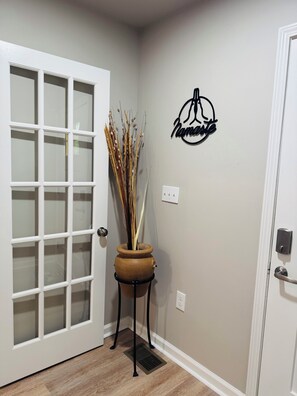 A hallway with a white door, a potted plant, and a wall-mounted sign. - Marvelous Townhome + Car Charger & Near Events (Atlanta)
