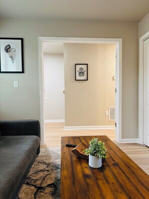 Ein Wohnzimmer mit einem dunkelgrauen Sofa, einem Couchtisch aus Holz mit einer Pflanze und einem gerahmten Bild an der Wand.