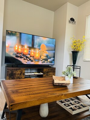 A wooden dining table with a television displaying a candlelit scene, a potted plant, and a decorative wooden tray with letters. - Marvelous Townhome + Car Charger & Near Events (Atlanta)