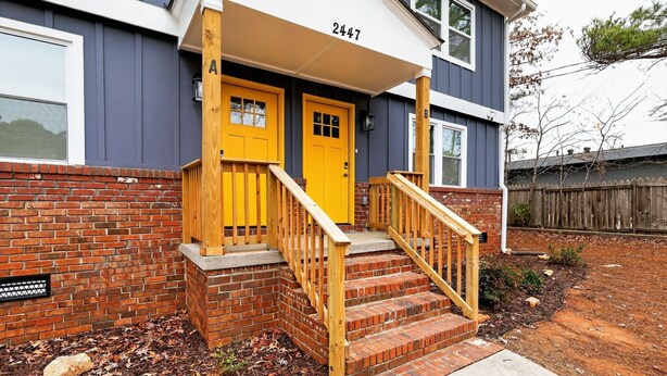 A two-story house with a yellow front door, a brick exterior, and a wooden staircase leading to the entrance. - Marvelous Townhome + Car Charger & Near Events (Atlanta)