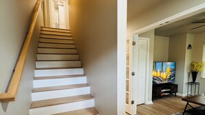 A staircase with wooden steps and white walls, leading to a room with a television and a plant. - Marvelous Townhome + Car Charger & Near Events (Atlanta)