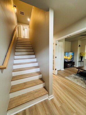 A staircase with wooden steps and white walls, leading to a room with a television and a plant. - Marvelous Townhome + Car Charger & Near Events (Atlanta)