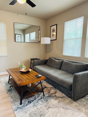 A living room with a wooden coffee table, a gray sofa, a floor lamp, and a large mirror on the wall. - Marvelous Townhome + Car Charger & Near Events (Atlanta)