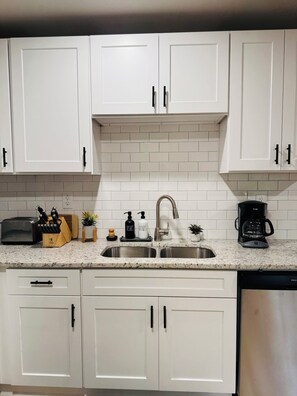 A kitchen with white cabinets, a stainless steel sink, a toaster, a coffee maker, and a knife block. - Marvelous Townhome + Car Charger & Near Events (Atlanta)