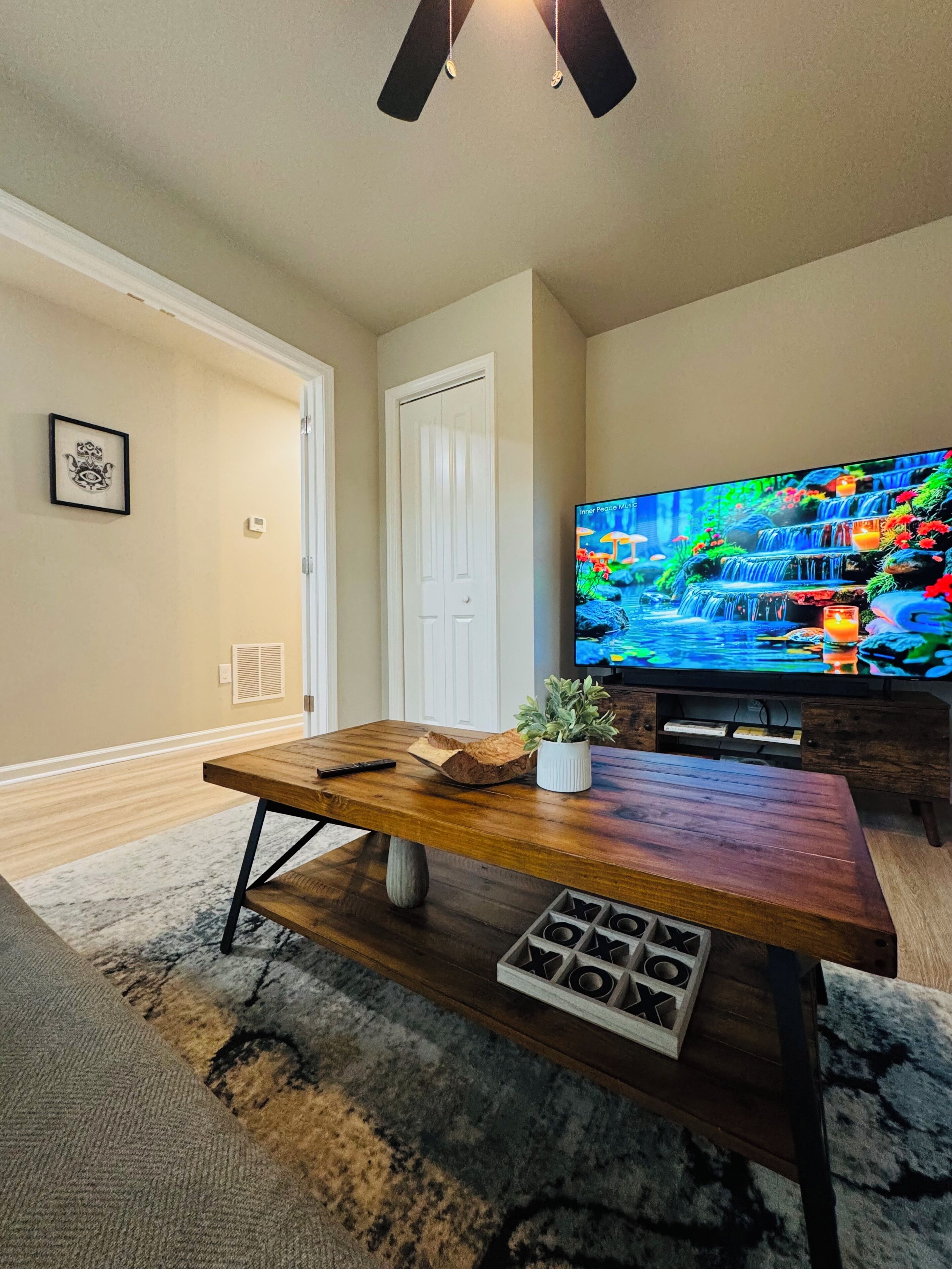 A living room with a wooden coffee table, a television displaying a nature scene, a white door, and a framed picture on the wall.