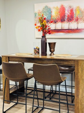 A dining area with a wooden table, two chairs, a vase with flowers, and a painting on the wall. - Marvelous Townhome + Car Charger & Near Events (Atlanta)