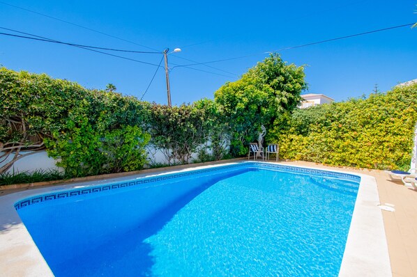 A clear blue swimming pool with a tiled edge, surrounded by lush greenery and a clear sky. - Casa do Livramento in Carvoeiro (Lagoa)