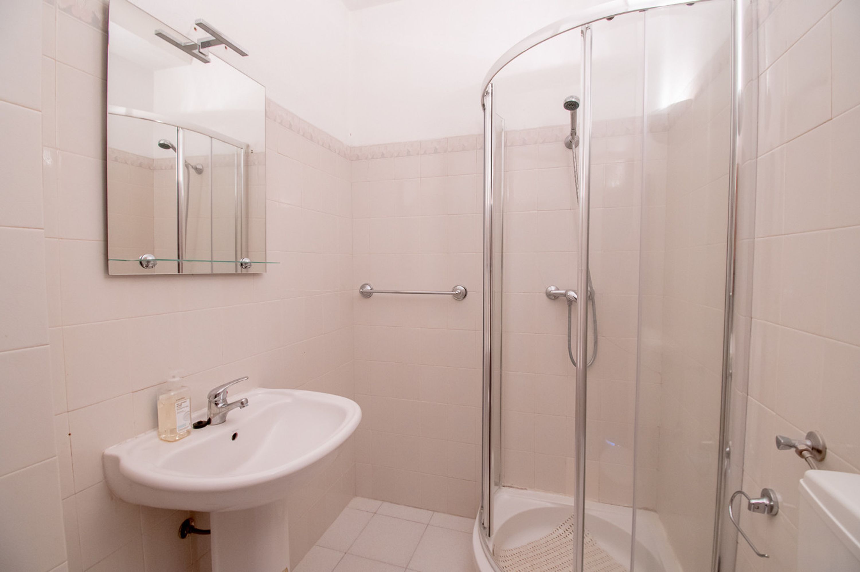 A bathroom with a glass-enclosed shower, a sink with a mirror above it, and a toilet.