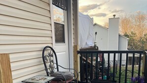 Eine überdachte Veranda mit Tisch und Stühlen, einem grün gemusterten Teppich und Topfpflanzen.