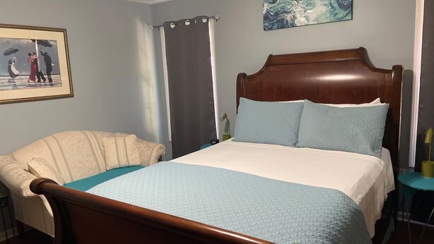 Ein Schlafzimmer mit einem hölzernen Bett, einem Sofa, einem Gemälde an der Wand und einem Vorhang.