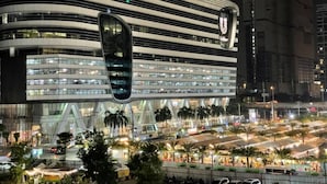 A modern building with a curved facade and multiple floors, surrounded by a bustling street and palm trees. - BIG Standing Desk with w/Pool, Spa, Gym, near MRT (Huai Khwang)