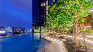 A rooftop pool with a city skyline in the background, surrounded by trees and wooden structures. - BIG Standing Desk with w/Pool, Spa, Gym, near MRT (Huai Khwang)