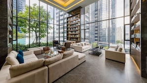 A spacious living room with large windows, a built-in bookshelf, and a modern sofa set. - BIG Standing Desk with w/Pool, Spa, Gym, near MRT (Huai Khwang)