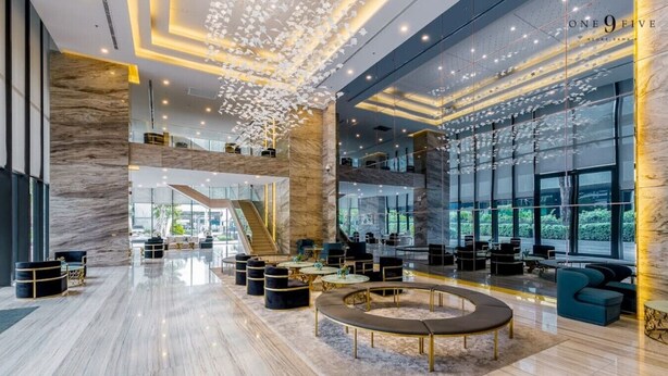 A spacious lobby with a central seating area, a staircase, and large windows offering views of greenery. - BIG Standing Desk with w/Pool, Spa, Gym, near MRT (Huai Khwang)