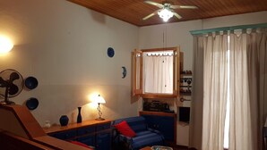 Una sala de estar acogedora con ventilador de techo, lámpara, sofá azul y ventana con cortinas.