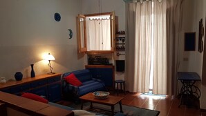 Una sala de estar con sofá, mesa, lámpara, radio y una ventana con cortinas.