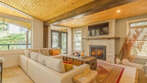 Ein gemütliches Wohnzimmer mit Kamin, Holzboden und großen Fenstern.
