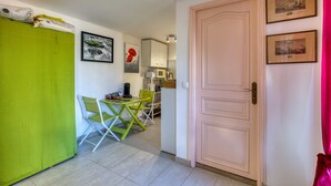 A compact living space with a kitchenette, a dining area with a green chair, and a closed door.