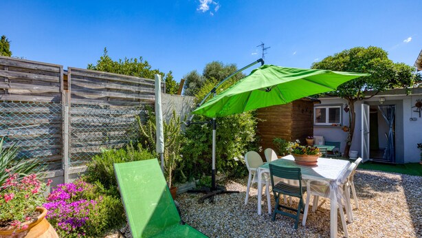 A patio with a table and chairs, a green umbrella, and a wooden fence.