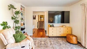 A living room with a sofa, a TV, a wooden cabinet, and a bookshelf. - Stunning fall foliage views with EV charger close to Cooperstown (Sharon Springs)